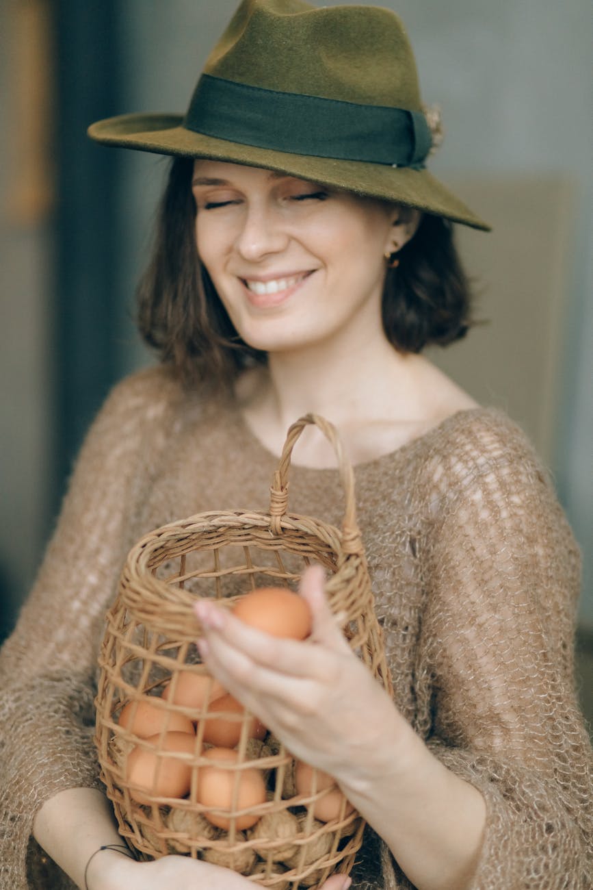 woman in fedora hat holding a basket with brown eggs
