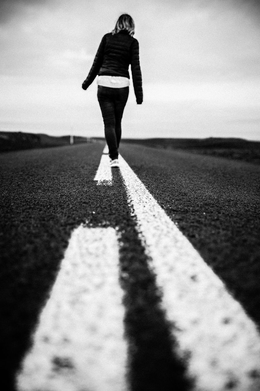 faceless woman walking on spotted line on asphalt road