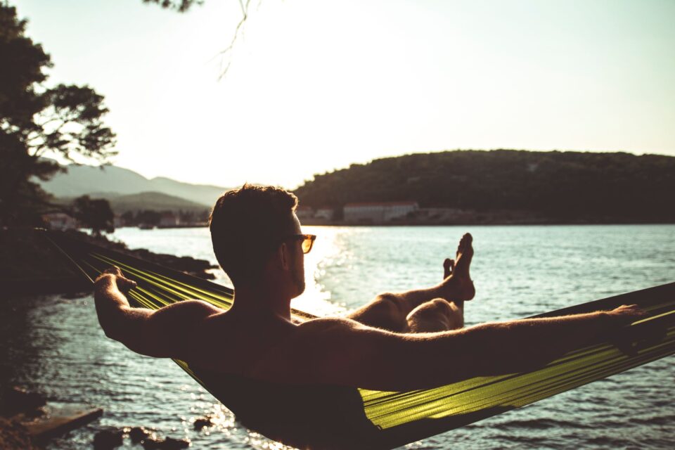 man sitting on hammock by the lake